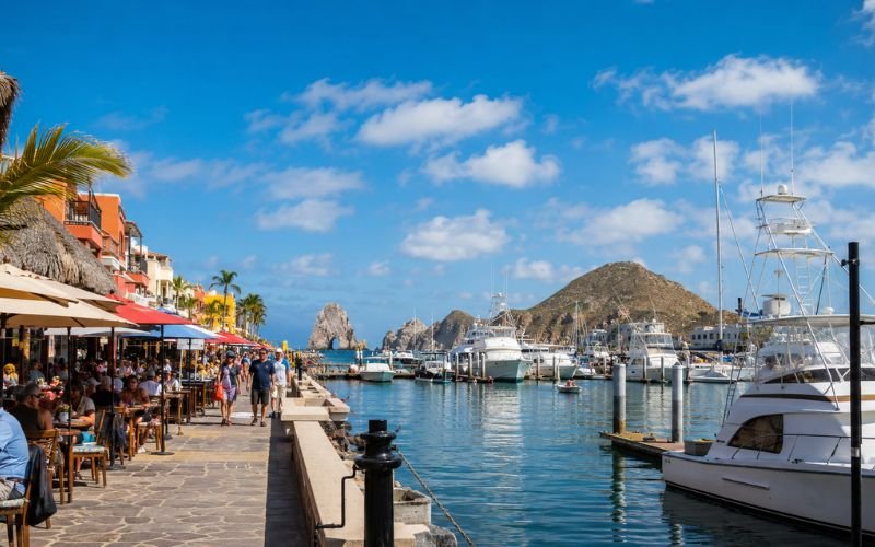 Panoramic view of Cabo San Lucas marina with waterfront bars, restaurants, and boats on a sunny day in Mexico