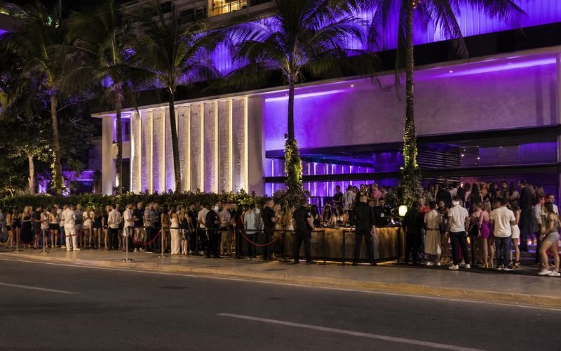 Long queue of tourists outside a busy nightclub on Cancun's Hotel Zone strip at night with security staff checking IDs